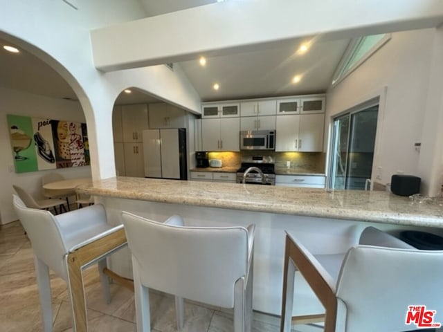 kitchen featuring light stone countertops, white cabinets, stainless steel appliances, decorative backsplash, and vaulted ceiling