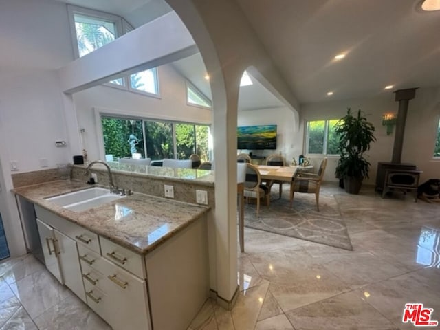 kitchen with sink, white cabinetry, light stone countertops, a wood stove, and high vaulted ceiling