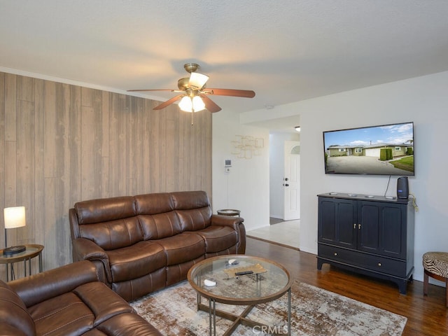 living room featuring ceiling fan, dark wood-type flooring, and wooden walls