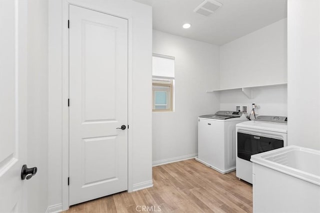 clothes washing area featuring light wood-type flooring, sink, and separate washer and dryer