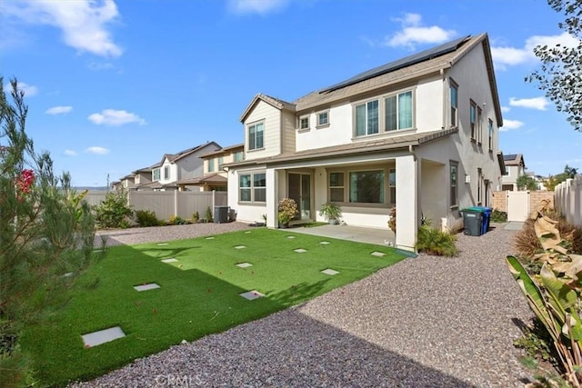 rear view of property with a patio area, a yard, central AC unit, and solar panels