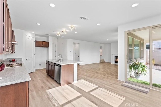 kitchen with light hardwood / wood-style floors, an island with sink, appliances with stainless steel finishes, light stone countertops, and sink