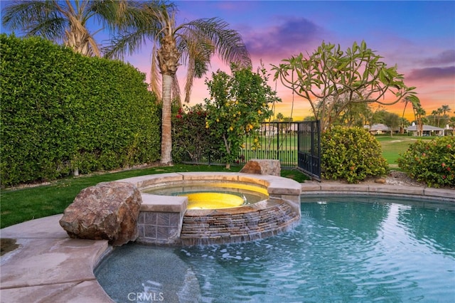 pool at dusk with an in ground hot tub and pool water feature