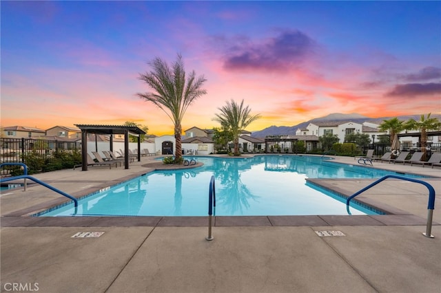 pool at dusk featuring a pergola and a patio