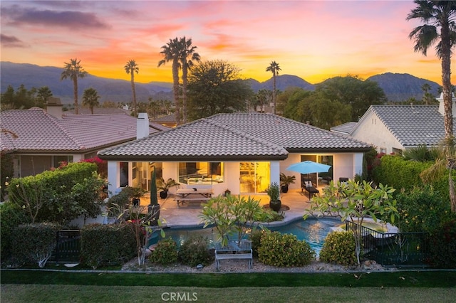 back house at dusk featuring a mountain view and a patio area