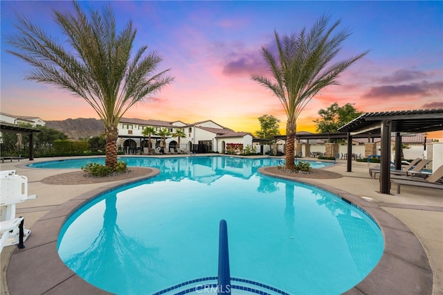 pool at dusk with a patio area and a pergola