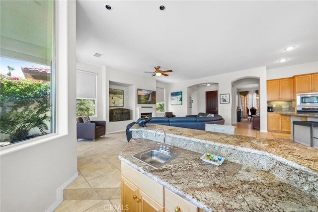 kitchen featuring stainless steel microwave, sink, decorative backsplash, light tile patterned floors, and ceiling fan