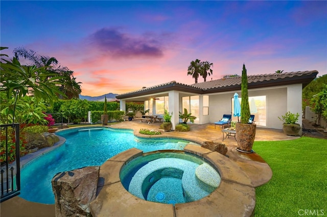 pool at dusk featuring an in ground hot tub and a patio