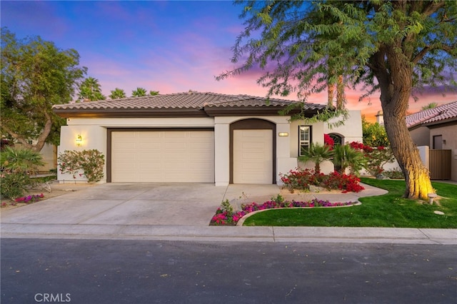 mediterranean / spanish home featuring driveway, an attached garage, a tiled roof, and stucco siding