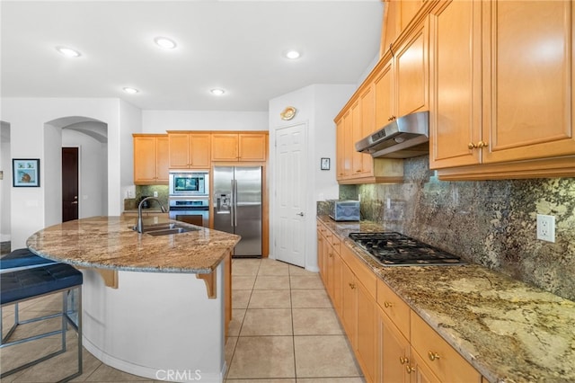 kitchen featuring light tile patterned flooring, appliances with stainless steel finishes, sink, decorative backsplash, and a center island with sink