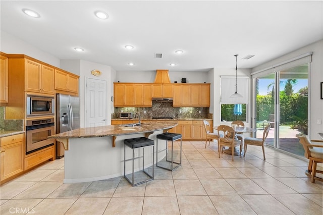 kitchen featuring appliances with stainless steel finishes, decorative light fixtures, sink, decorative backsplash, and a kitchen island with sink