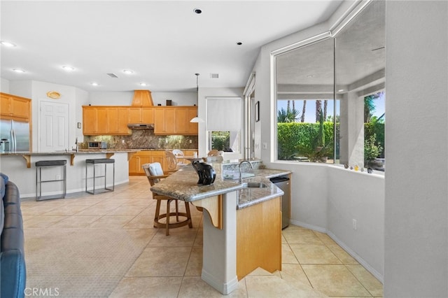 kitchen with appliances with stainless steel finishes, an island with sink, a kitchen bar, decorative light fixtures, and light tile patterned flooring