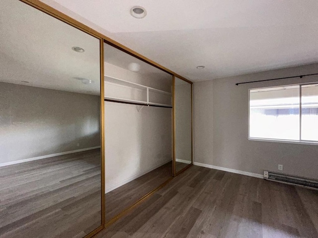 unfurnished bedroom featuring a baseboard heating unit, dark hardwood / wood-style floors, and a closet