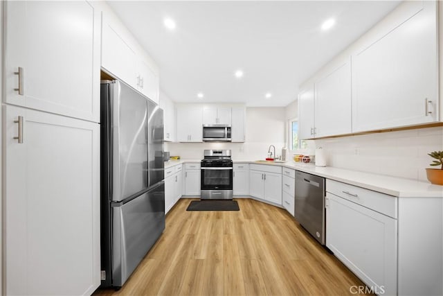 kitchen featuring white cabinetry, stainless steel appliances, backsplash, light wood-type flooring, and sink