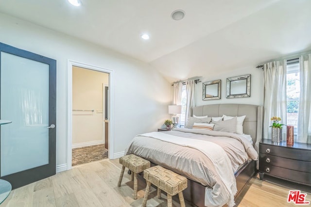 bedroom with a walk in closet, lofted ceiling, light hardwood / wood-style floors, and multiple windows