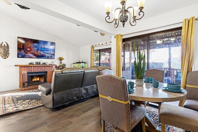 dining space featuring a textured ceiling, a fireplace, an inviting chandelier, dark hardwood / wood-style floors, and vaulted ceiling