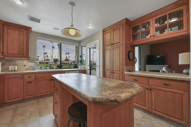 kitchen with a kitchen island, decorative light fixtures, tasteful backsplash, sink, and light tile patterned floors