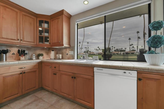 kitchen with light tile patterned floors, tile countertops, tasteful backsplash, dishwasher, and sink