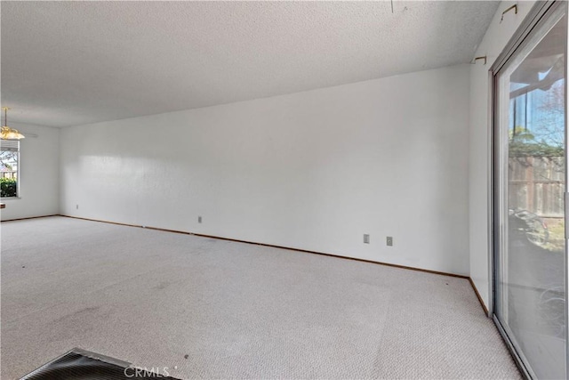 empty room featuring light colored carpet, a textured ceiling, and baseboards