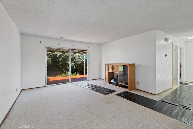 unfurnished living room featuring a textured ceiling, carpet flooring, and visible vents