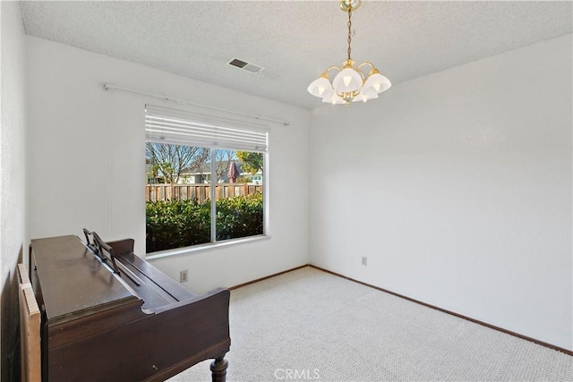 unfurnished office featuring visible vents, an inviting chandelier, carpet flooring, a textured ceiling, and baseboards