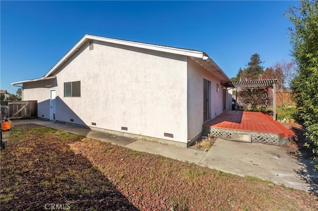 view of property exterior with crawl space, fence, a wooden deck, a pergola, and stucco siding