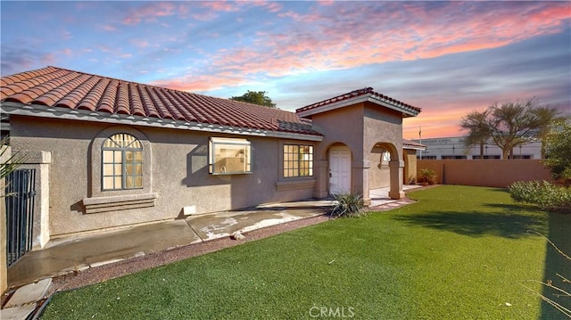 back house at dusk featuring a patio area and a lawn