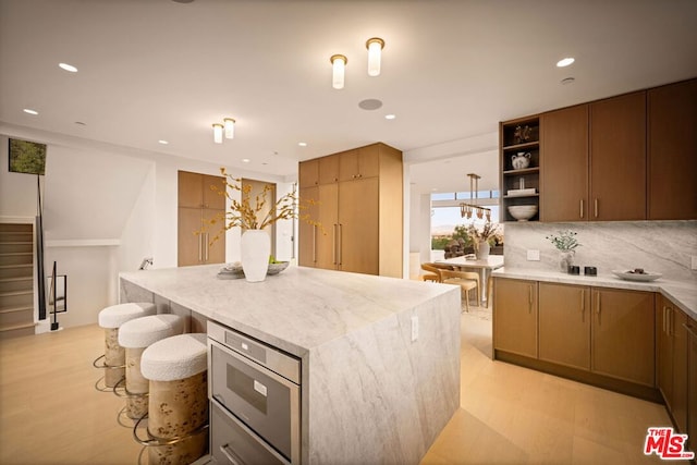 kitchen with a center island, decorative backsplash, light hardwood / wood-style floors, a breakfast bar area, and built in microwave