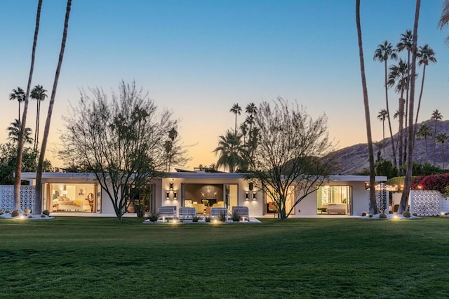 back house at dusk with an outdoor living space and a lawn