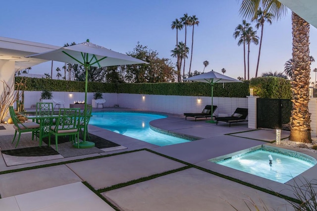 pool at dusk with a patio area and a hot tub