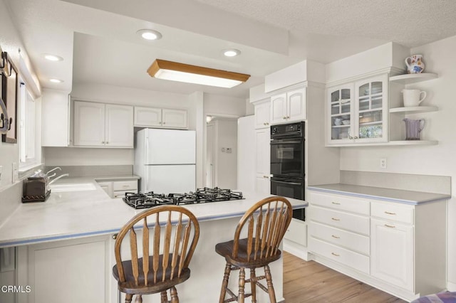 kitchen featuring stainless steel gas stovetop, kitchen peninsula, a kitchen breakfast bar, white cabinets, and white refrigerator