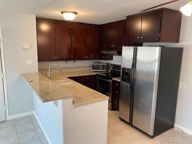 kitchen featuring light tile patterned floors, kitchen peninsula, appliances with stainless steel finishes, dark brown cabinets, and sink