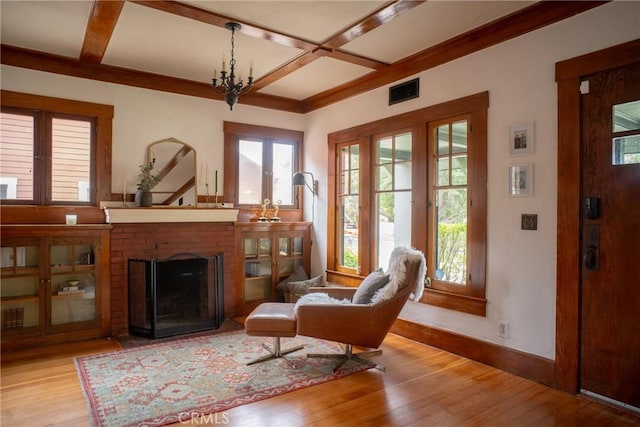 sitting room featuring a fireplace, an inviting chandelier, light wood-type flooring, beam ceiling, and coffered ceiling