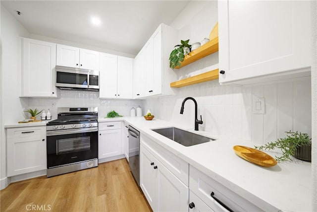 kitchen featuring appliances with stainless steel finishes, sink, light wood-type flooring, white cabinets, and decorative backsplash