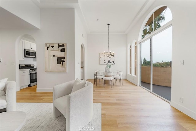 living room featuring ornamental molding, light hardwood / wood-style floors, a high ceiling, and an inviting chandelier