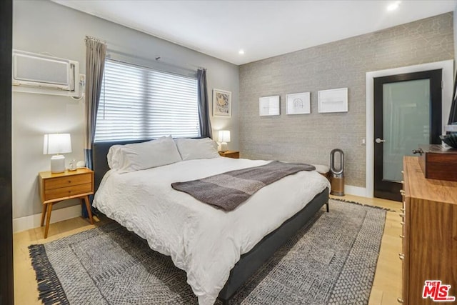 bedroom with a wall mounted AC and light hardwood / wood-style floors