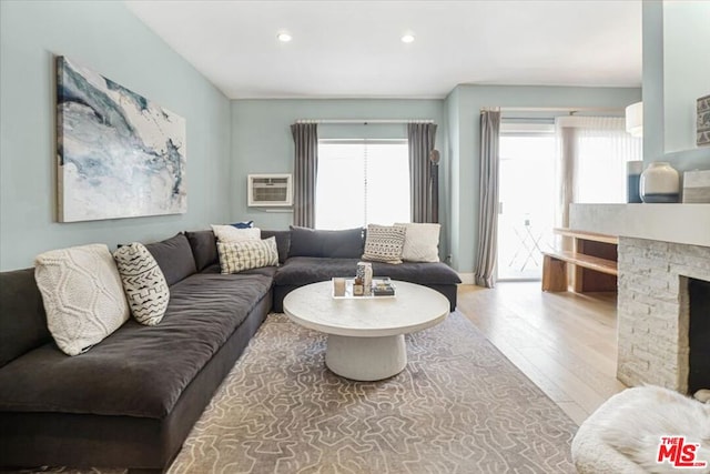 living room featuring a wall unit AC, a fireplace, and light hardwood / wood-style flooring