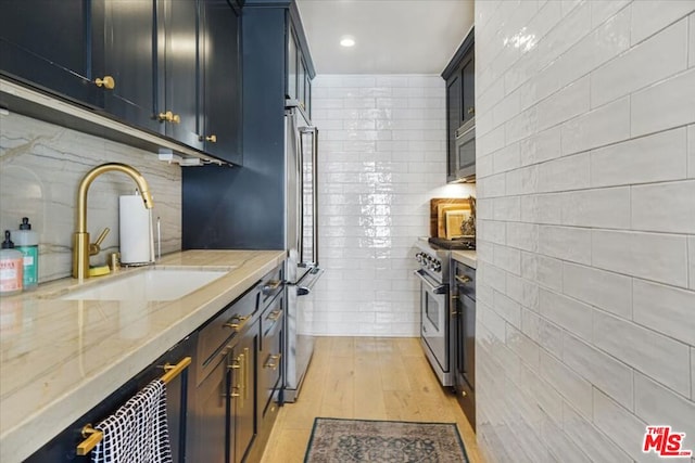 kitchen featuring light hardwood / wood-style floors, appliances with stainless steel finishes, tile walls, light stone counters, and sink