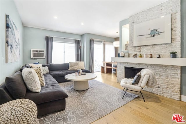 living room featuring hardwood / wood-style floors, a stone fireplace, and a wall mounted air conditioner