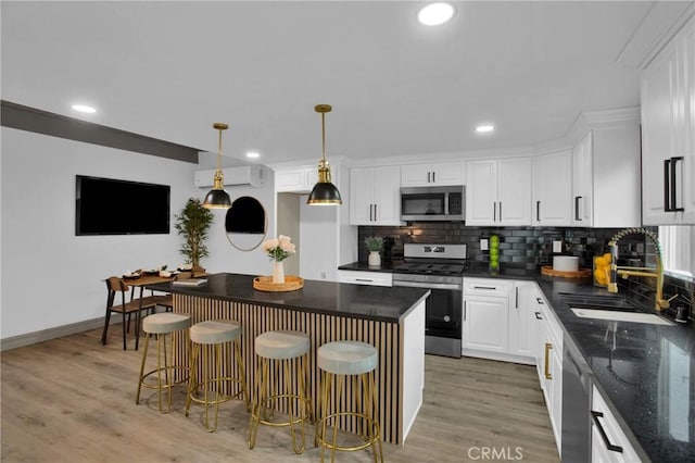 kitchen featuring stainless steel appliances, sink, decorative light fixtures, white cabinetry, and a kitchen bar