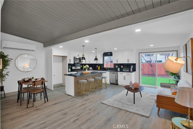 kitchen with stainless steel appliances, white cabinetry, beamed ceiling, an AC wall unit, and a kitchen bar