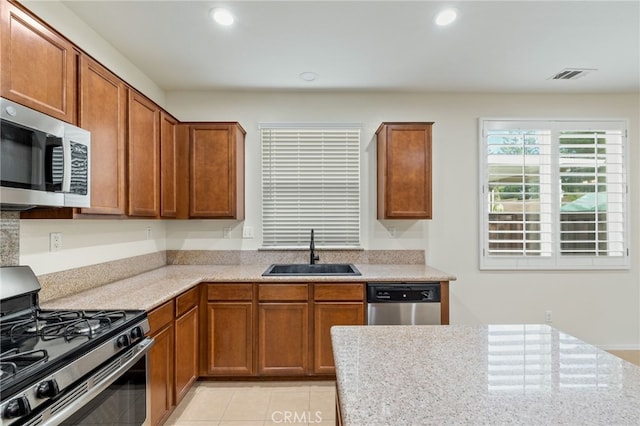 kitchen featuring light tile patterned floors, appliances with stainless steel finishes, light stone counters, and sink