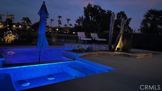 pool at dusk featuring a patio area and an in ground hot tub