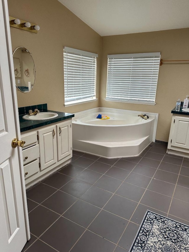 bathroom featuring lofted ceiling, vanity, tile patterned flooring, and a bathing tub