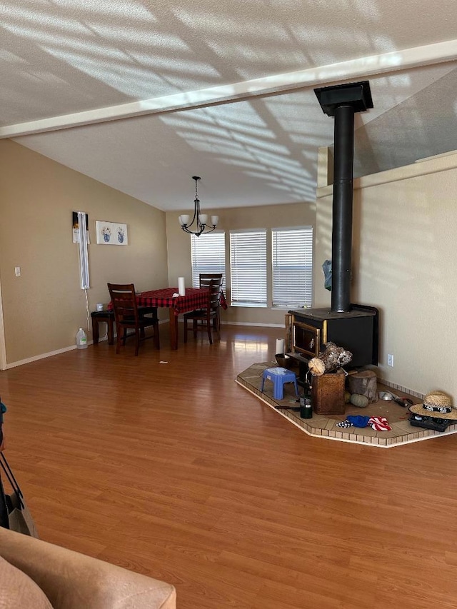 living room with a wood stove, wood-type flooring, a chandelier, and vaulted ceiling