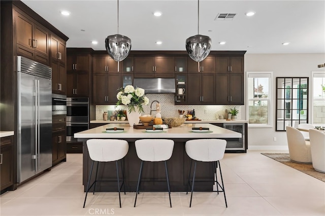 kitchen with hanging light fixtures, appliances with stainless steel finishes, and a center island with sink