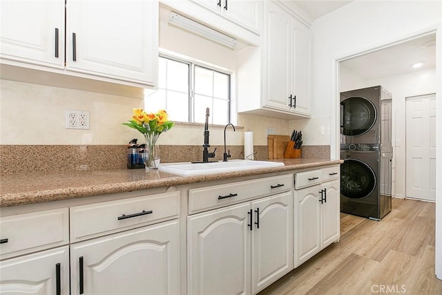 kitchen featuring white cabinetry, light hardwood / wood-style floors, stacked washer / dryer, and sink