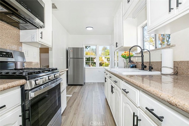 kitchen with light hardwood / wood-style floors, sink, appliances with stainless steel finishes, white cabinets, and light stone counters