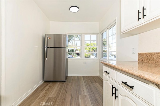 kitchen with light stone countertops, white cabinets, stainless steel fridge, and plenty of natural light