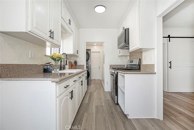 kitchen featuring stainless steel appliances, a barn door, white cabinetry, and sink